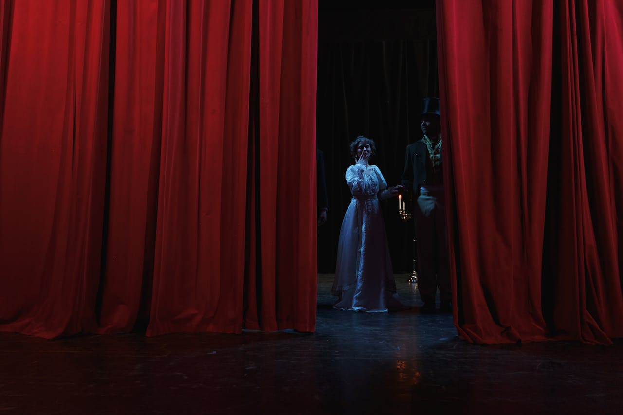 Dramatic stage scene with actors behind red curtains, creating a theatrical ambiance.