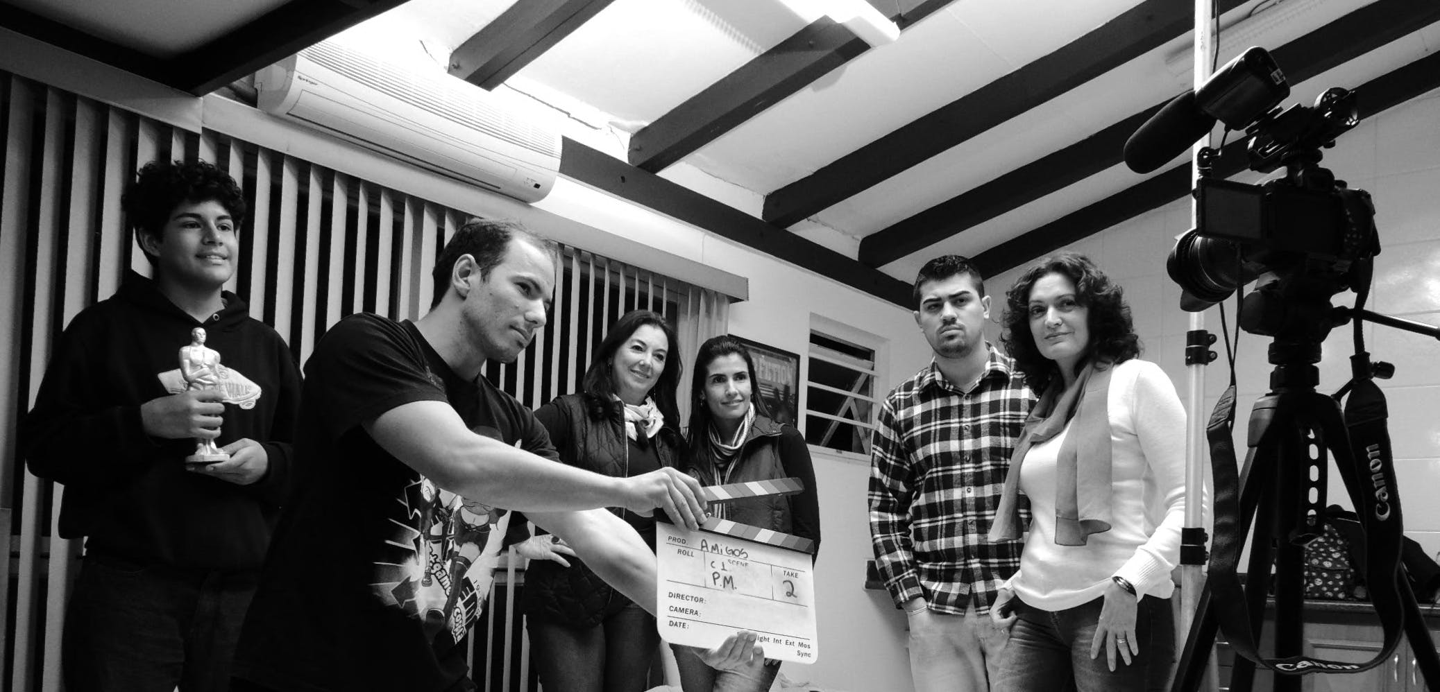 A group of adults collaborate on a filmmaking project, seen holding a clapperboard indoors.